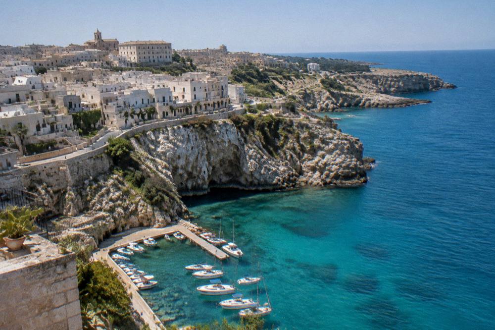 Aerial view of a white clifftop town above a turquoise cove on the Salento Adriatic coast