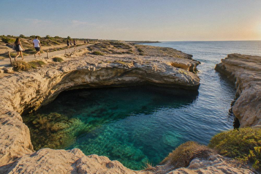 Visitors walking on a limestone path above a coastal sinkhole pool on a sunny afternoon