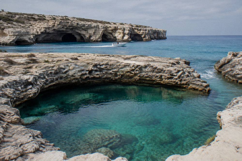A small boat cruising along a cliff face with sea caves near white limestone rocks