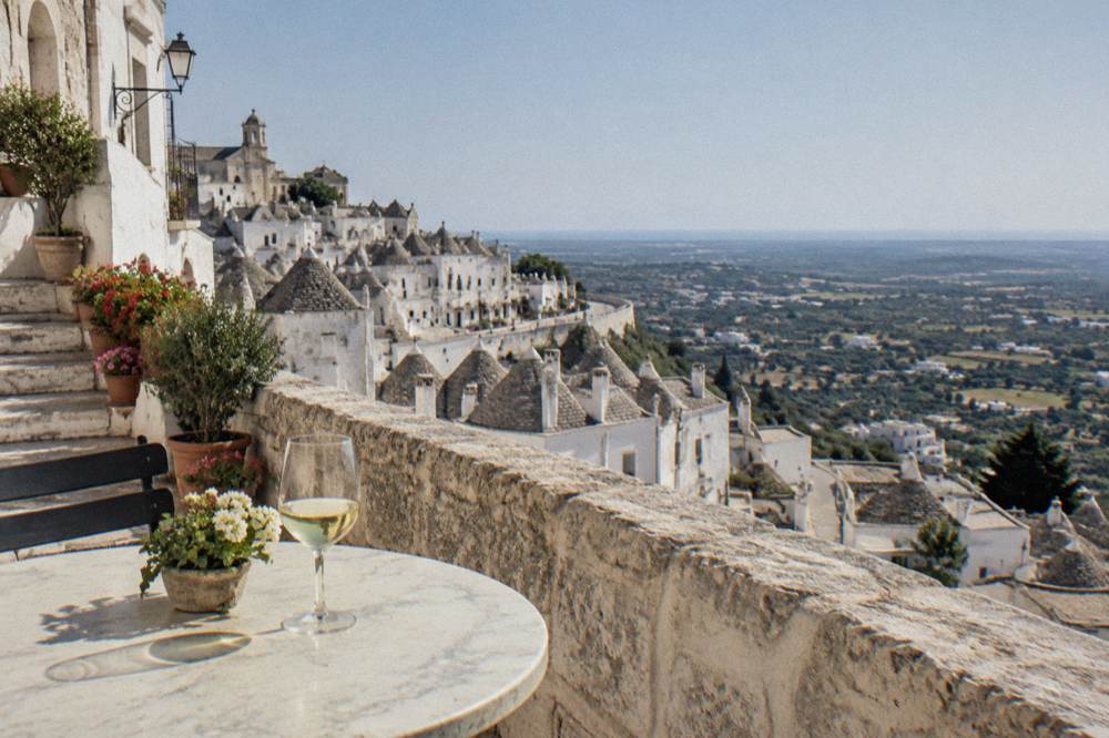 Outdoor table with a glass of white wine overlooking the valley in Locorotondo