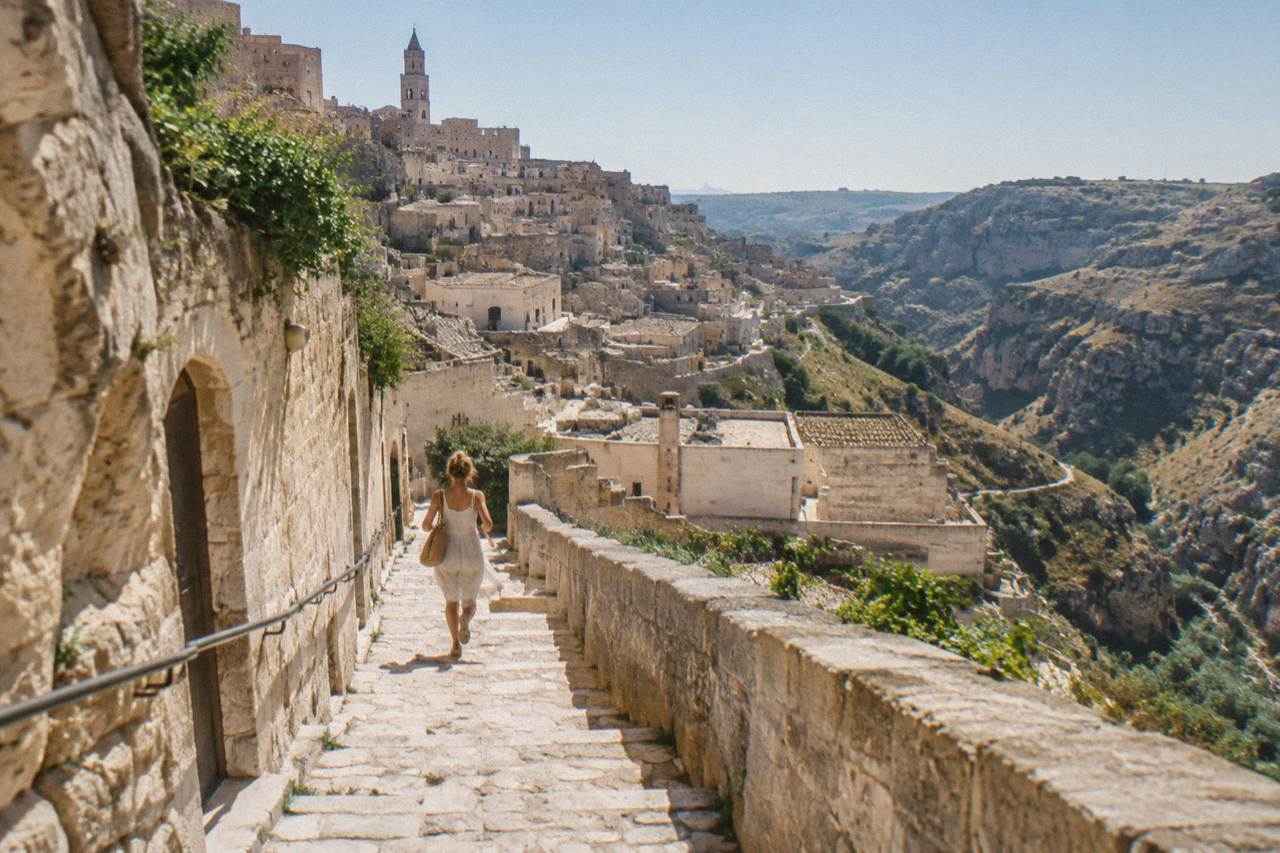 A hillside town of pale stone cave dwellings stacked above a ravine under a clear sky