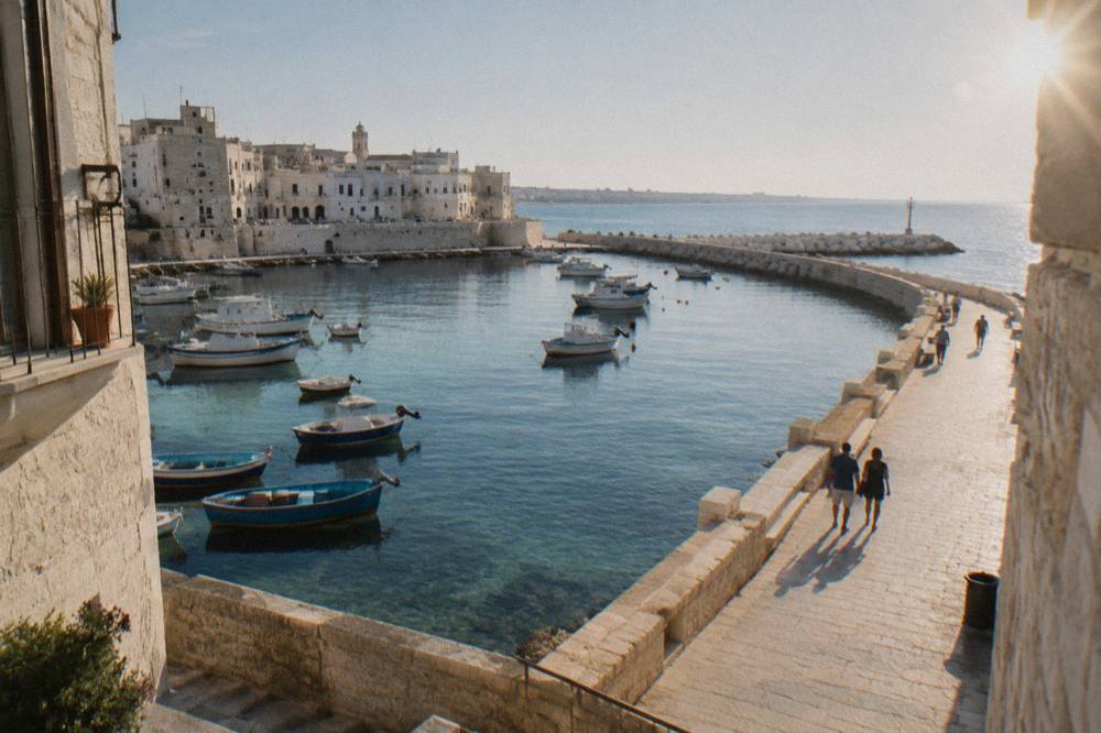 A pale stone seafront promenade curving beside a calm blue bay at midday