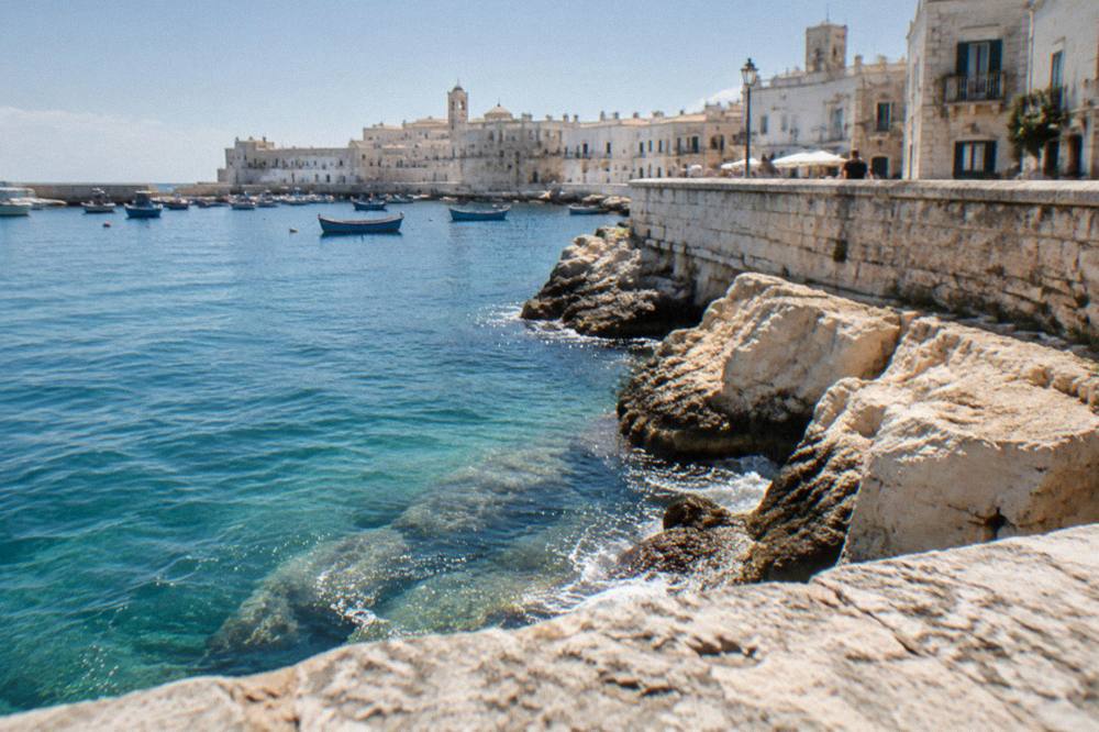 Turquoise water breaking against pale limestone rocks below a low sea wall