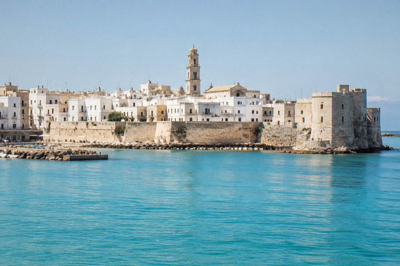 The white-walled houses and rooftops of Otranto old town seen from the sea, with the cathedral bell tower rising above the buildings