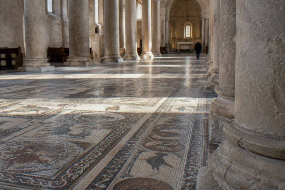 The interior of Otranto Cathedral with the medieval mosaic floor stretching down the nave beneath stone columns