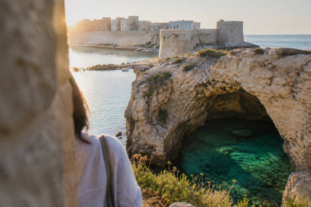 A sea cave opening in limestone cliffs with clear green water visible inside the arch