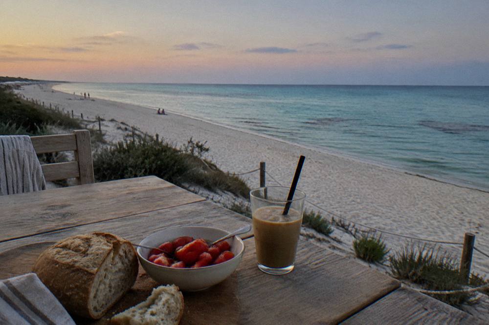Simple beach lunch of bread, tomatoes and iced coffee on a wooden table by the sea