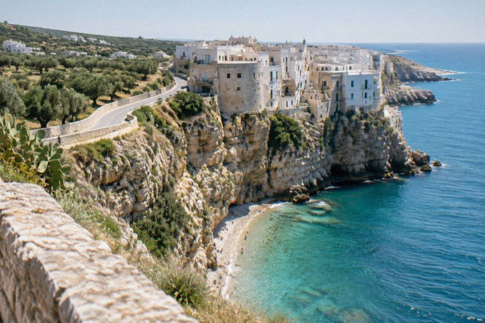 A coastal road winding north through olive groves in Puglia toward the sea