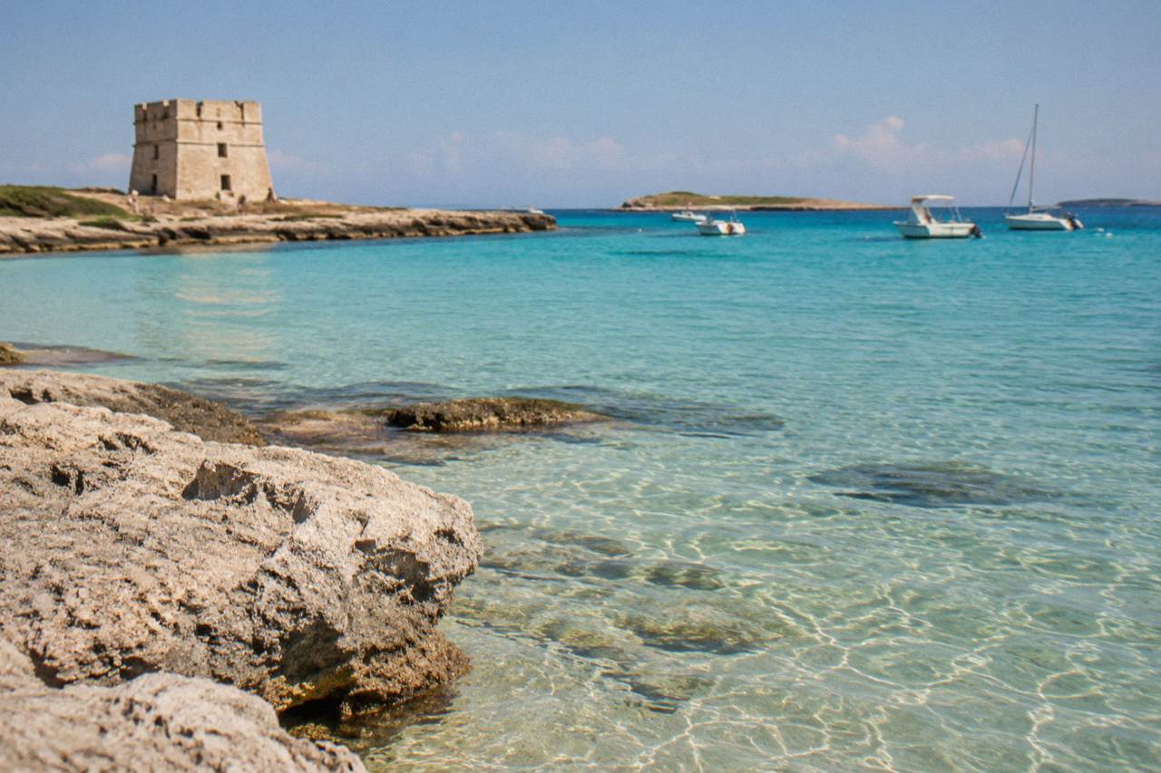 Turquoise shallow water over sand at a Porto Cesareo beach with small boats anchored offshore