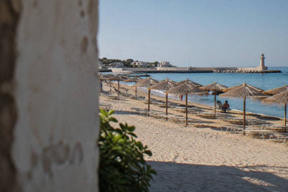 A sandy beach with rows of sunbeds and straw umbrellas along the waterline