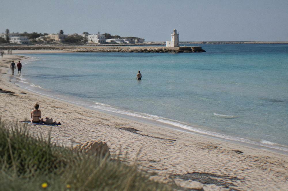 Shallow turquoise water over sand with a distant harbour wall
