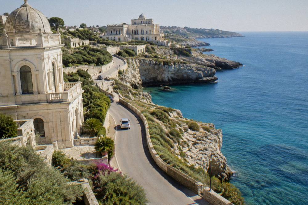 A narrow coastal road curving along a cliff with the sea beyond