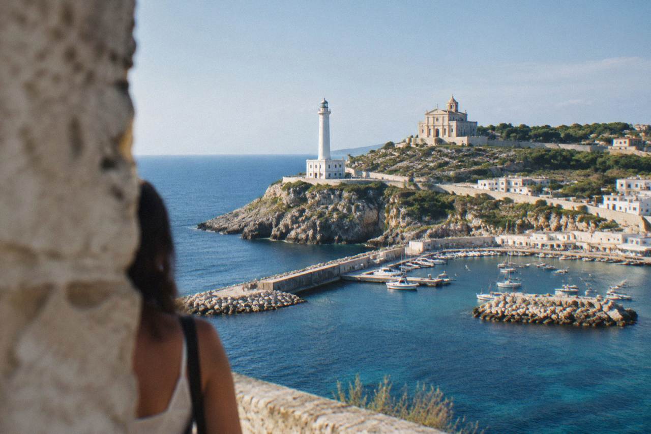 A white lighthouse and basilica standing above a small harbour at the southern tip of Salento
