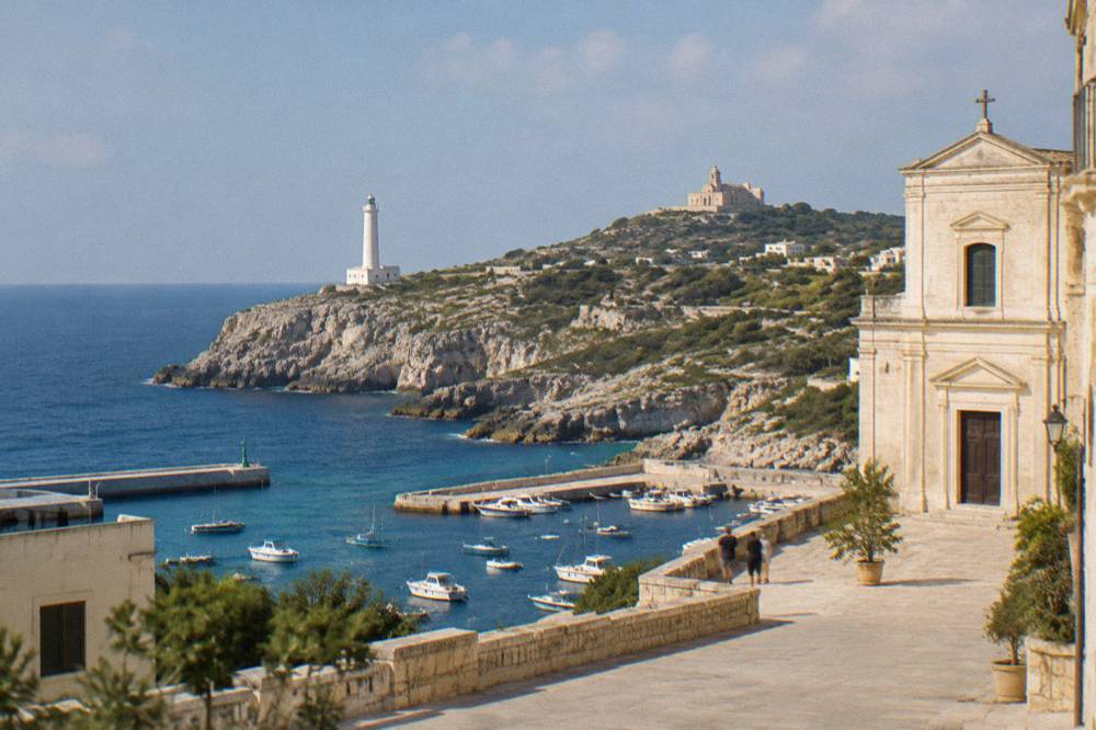 A pale seaside basilica with a square facade seen from a sunlit square above the sea