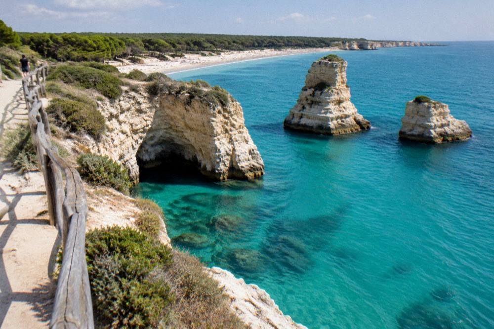A limestone cliff top path above a flooded sea cave with pale blue water
