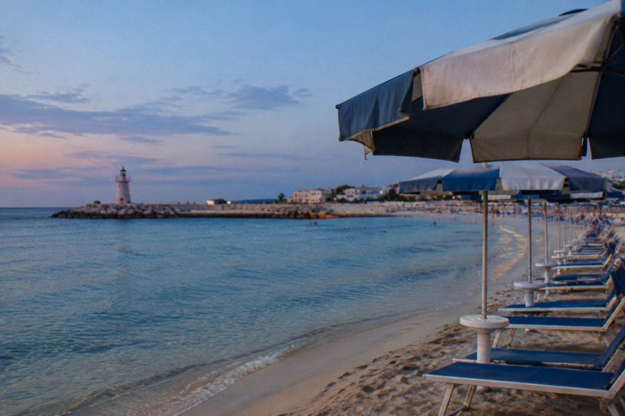 A sandy beach with clear shallow water and a row of sun umbrellas on the Salento coast