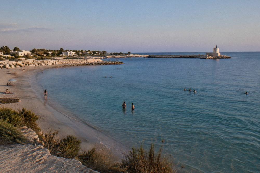 People swimming in calm clear water over sand on a warm September day