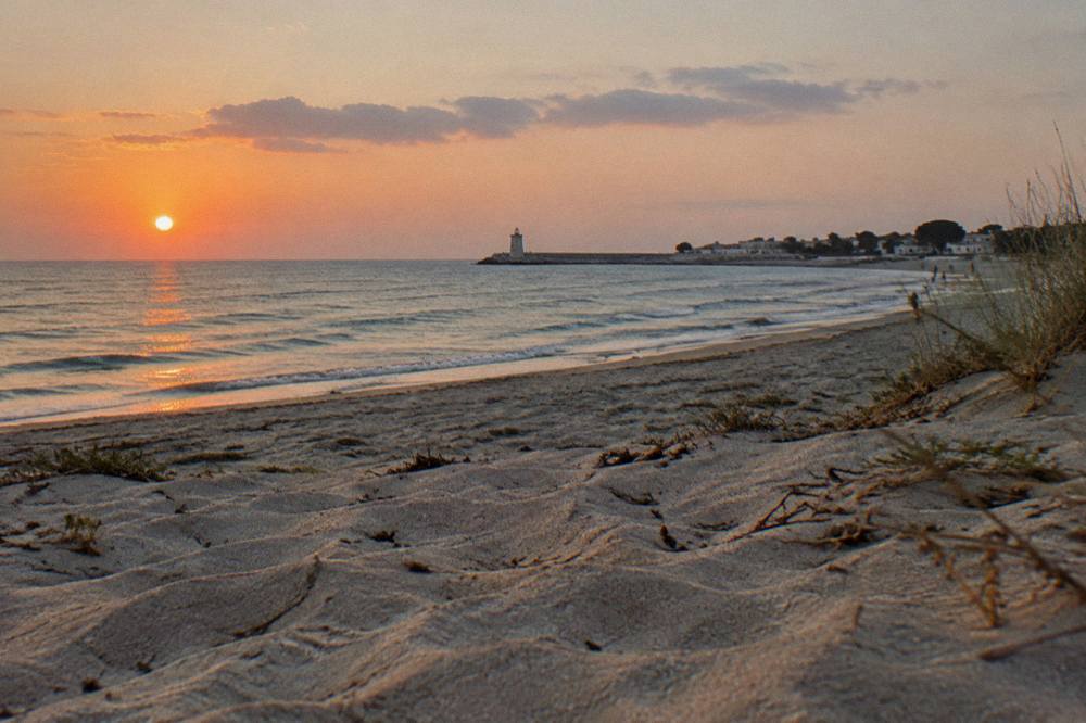 A sunset over the Ionian sea seen from a sandy Salento beach with dunes