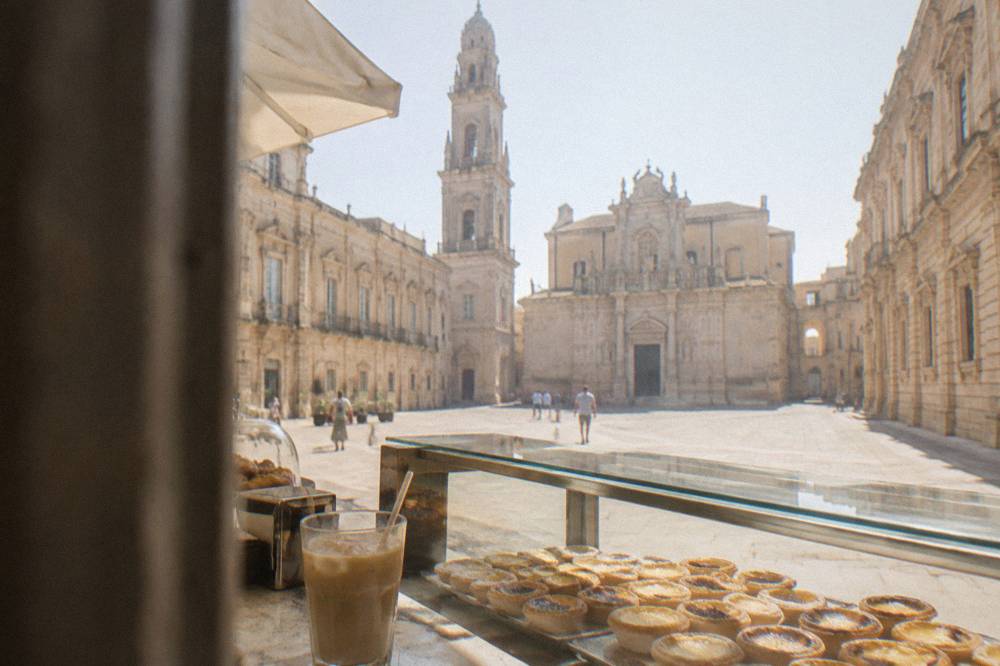 A pastry counter with rows of small custard tarts and a cup of iced coffee with milk beside them.