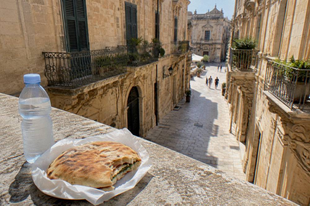 A simple lunch of a round stuffed flatbread and a bottle of water on a stone ledge in an old town street.