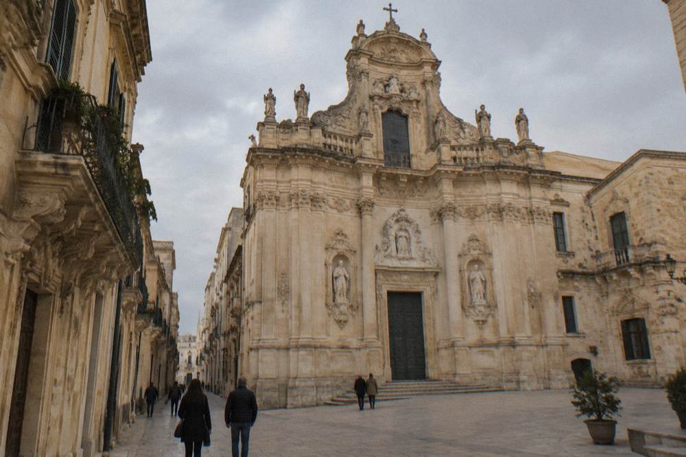 A Lecce church facade in warm autumn afternoon light with a few people walking below
