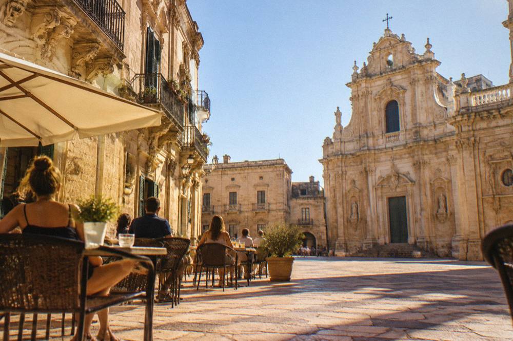 People seated at outdoor cafe tables on a Lecce piazza in warm evening light