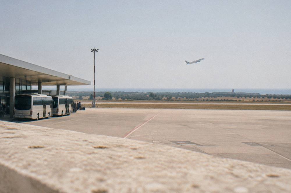 A plane climbing over flat farmland near a coastal airport in Puglia