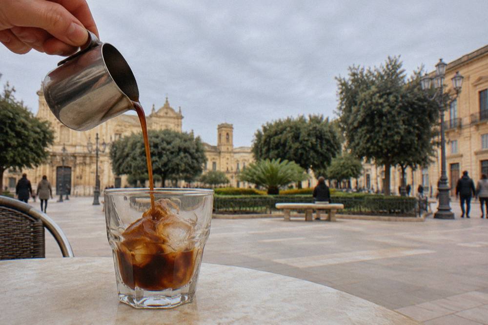 Close view of espresso being poured over ice cubes in a small glass