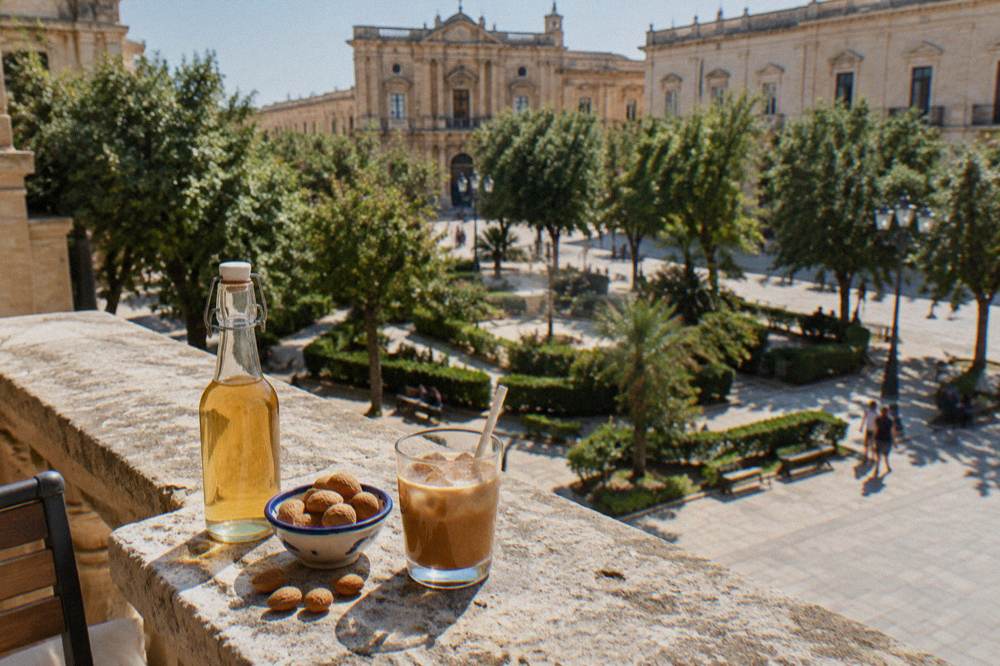 Almonds and a bottle of almond syrup beside a glass of iced coffee