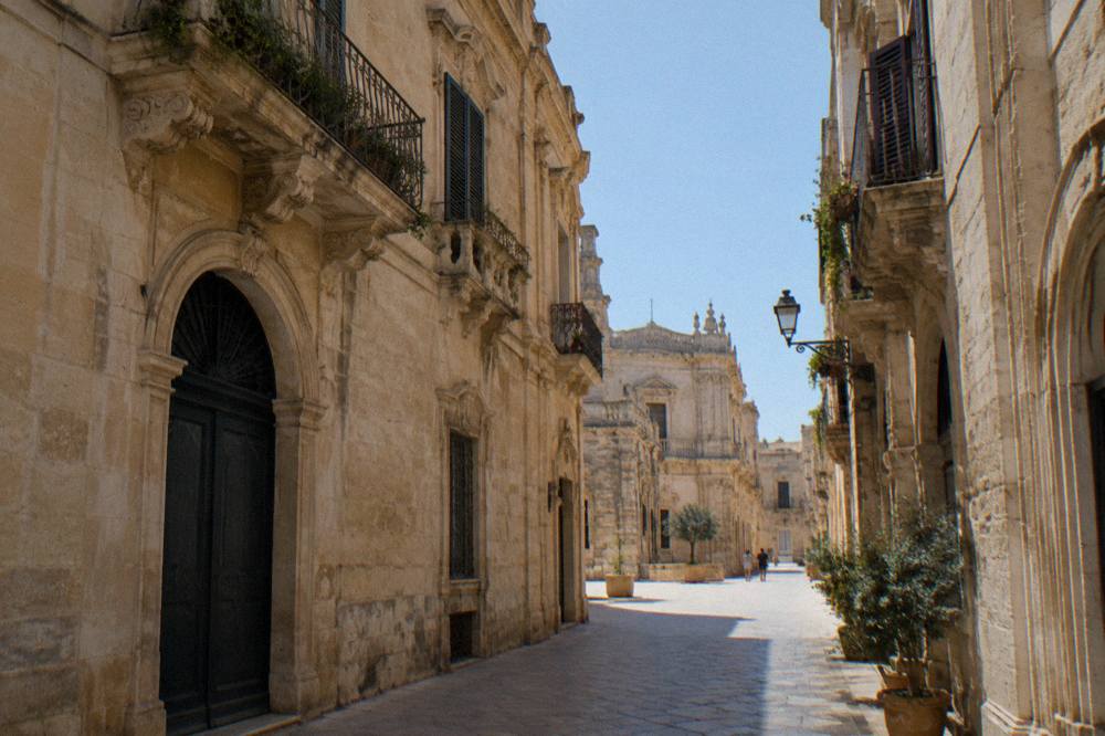 A shaded narrow street with limestone buildings in Lecce old town on a warm day