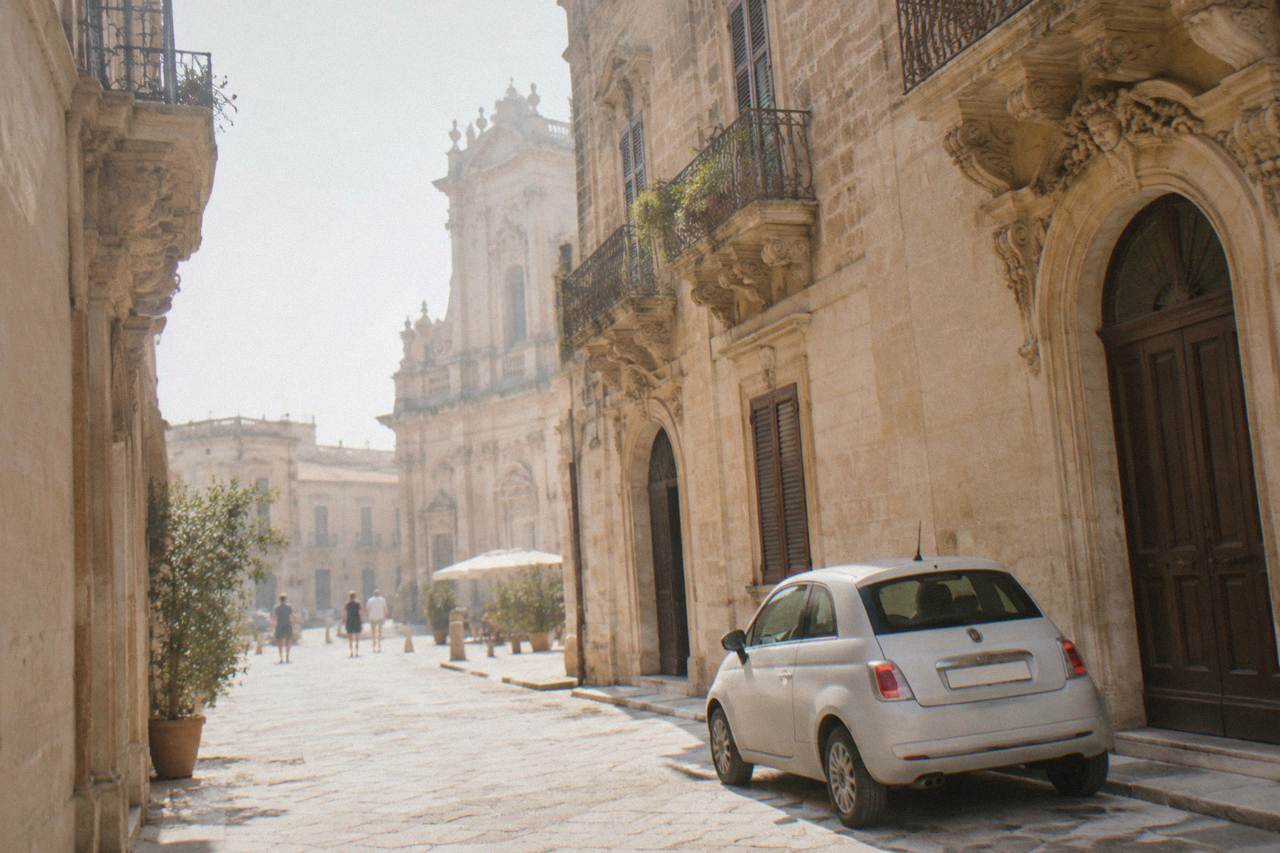 A small rental car parked on a sunlit limestone street beside baroque buildings in Lecce