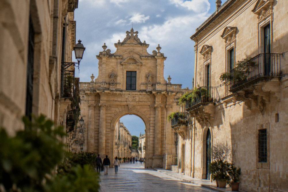A white-walled hilltop town with narrow streets seen from a country road in Puglia