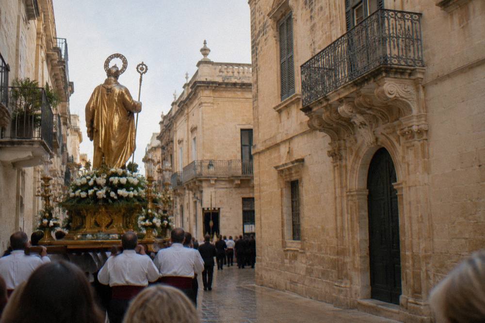 A gilded saint statue carried on a platform through a baroque street