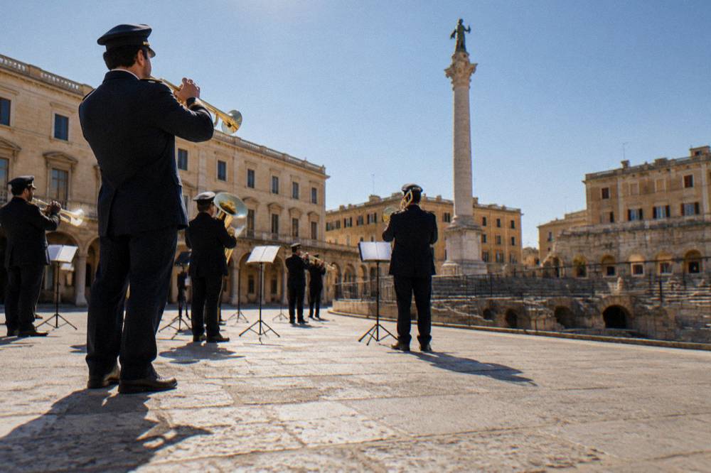 A band in uniform playing brass instruments in a floodlit square