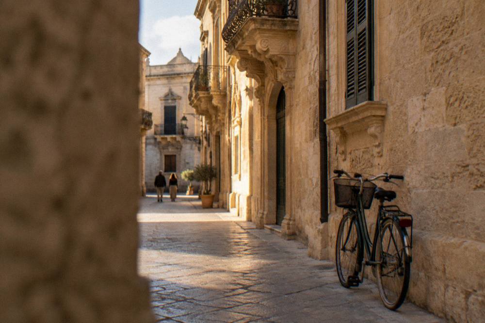 A bicycle leaning against a limestone wall on a quiet street in Lecce at golden hour