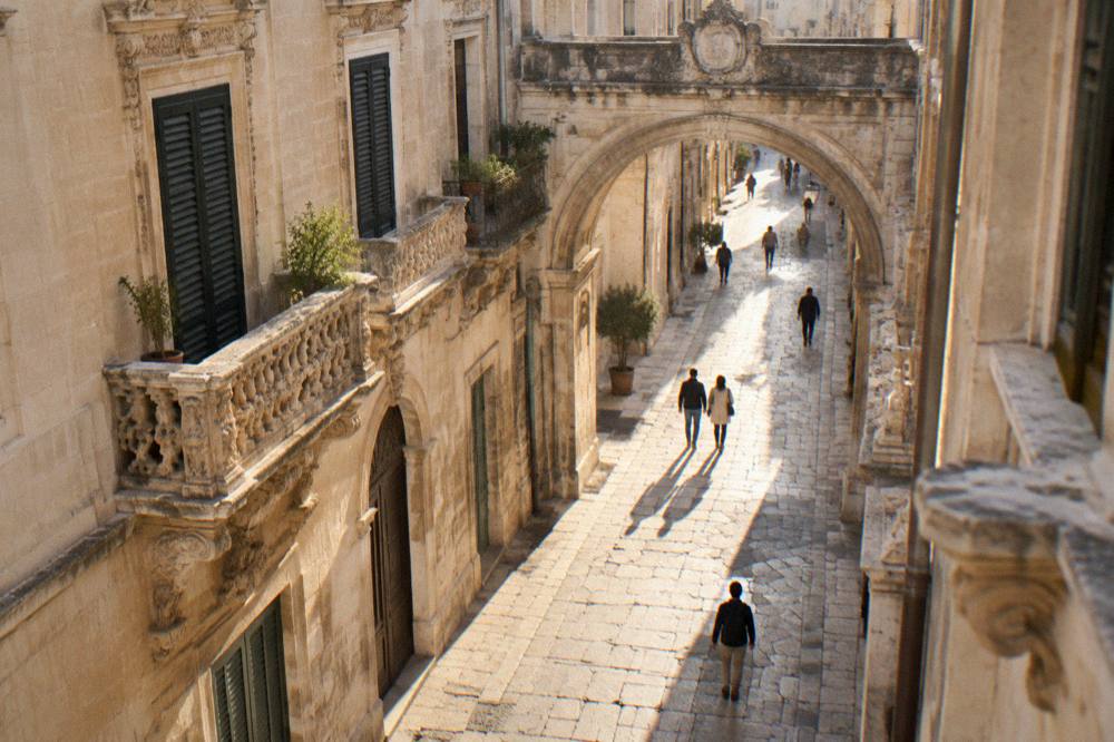 A narrow stone-paved street in Lecce with a historic gate arch spanning it