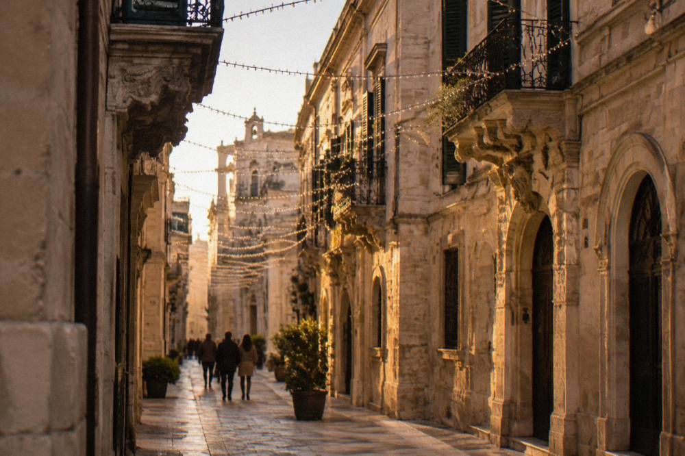 Strings of white Christmas lights arching over a narrow street of limestone buildings in Lecce