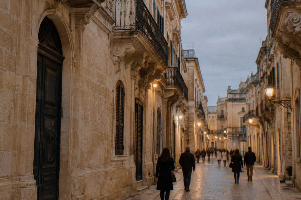 People strolling down a lit Lecce shopping street at dusk past closed baroque facades