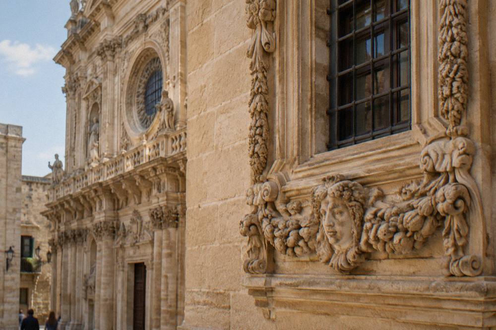 Close view of a carved limestone window frame with garlands and a stylised face