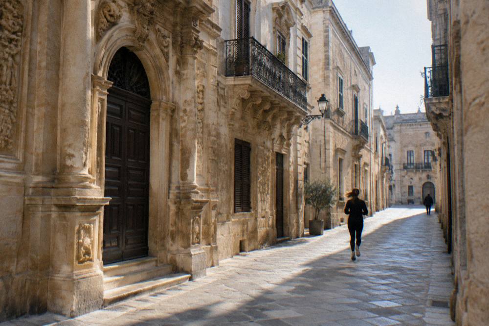 Golden pietra leccese facade detail with carved columns and a balcony in Lecce