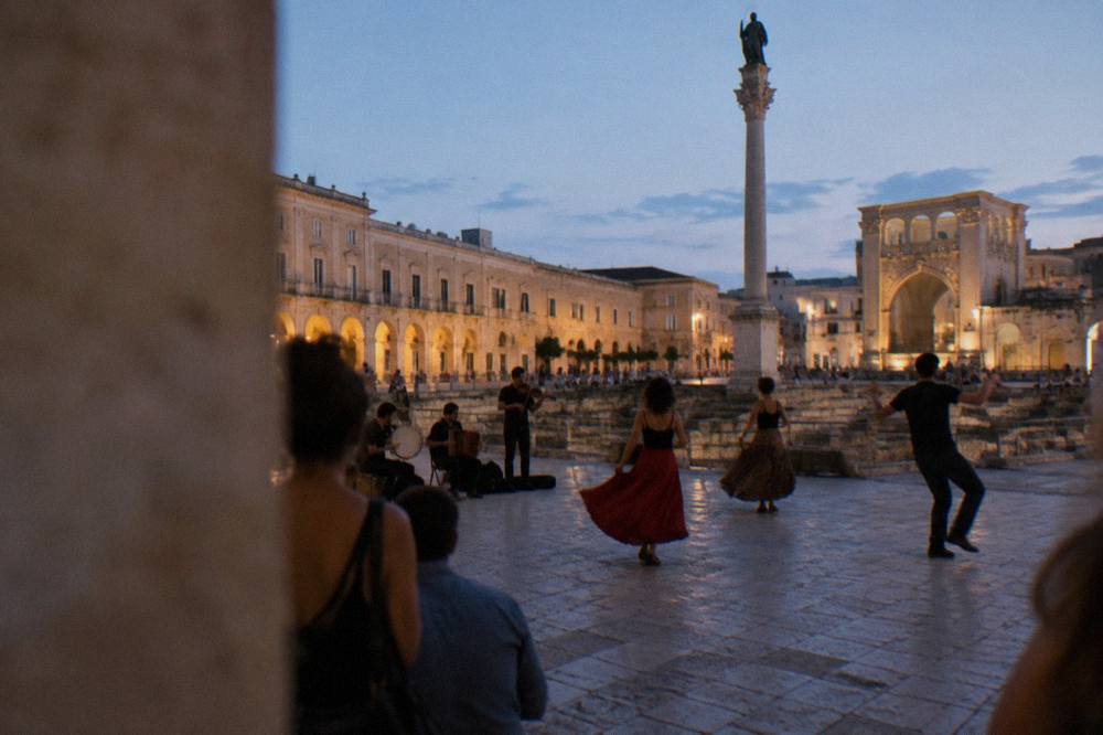 A band playing pizzica music with dancers in an Italian town square at dusk