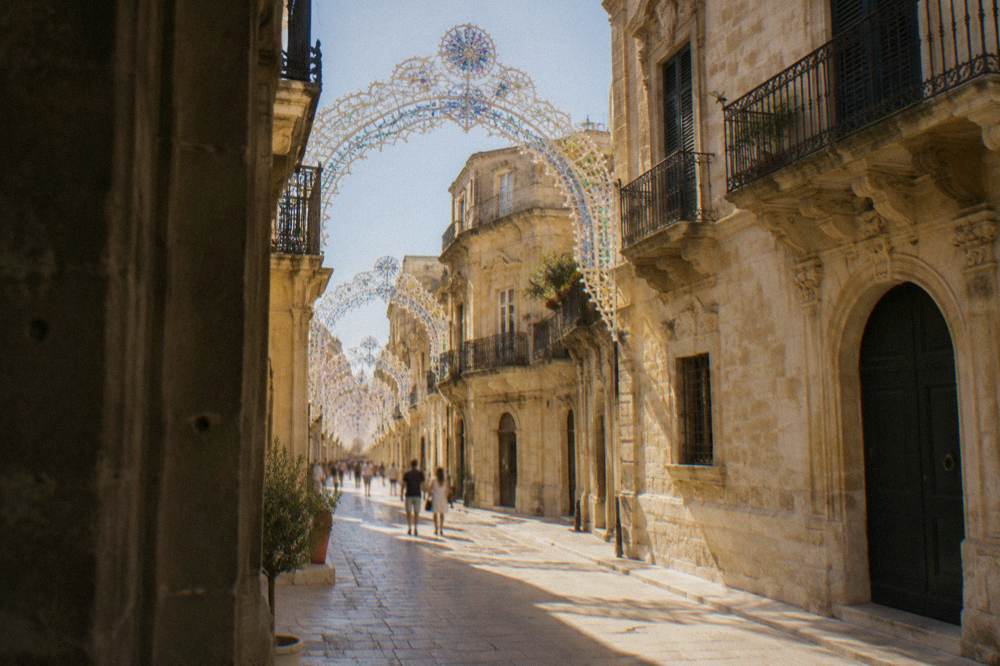 Illuminated light arches over a street of baroque buildings during an Italian patron saint festival
