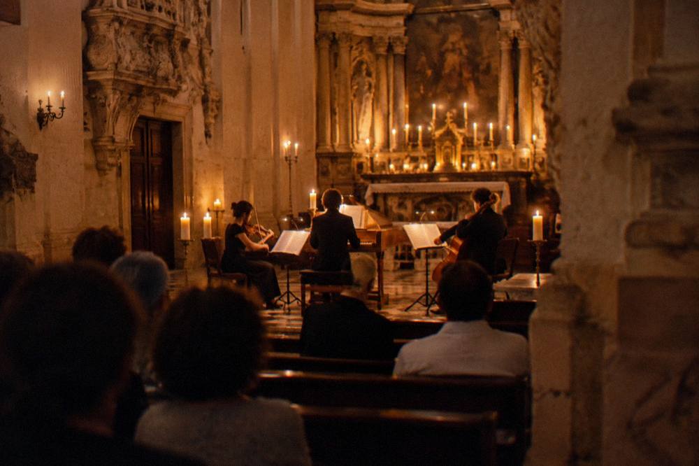 Musicians performing inside a candlelit baroque church during an evening concert