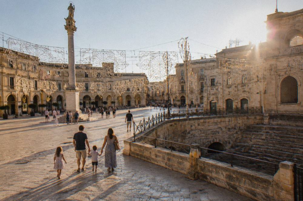 A family walking through a decorated Italian city square with festival lights strung overhead