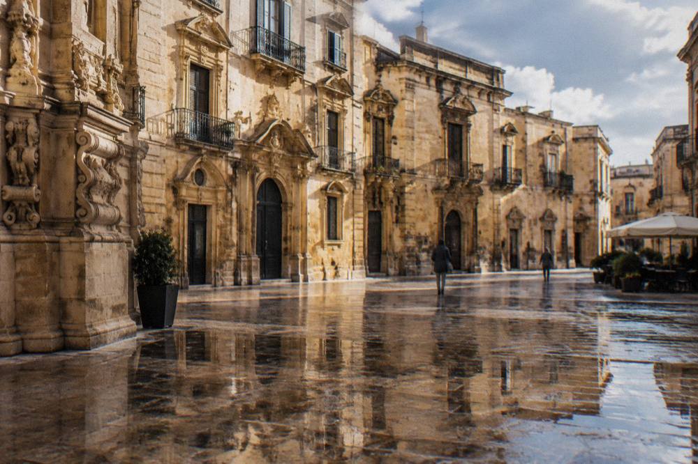 Wet cobblestones in a Lecce square reflecting baroque building facades after rain