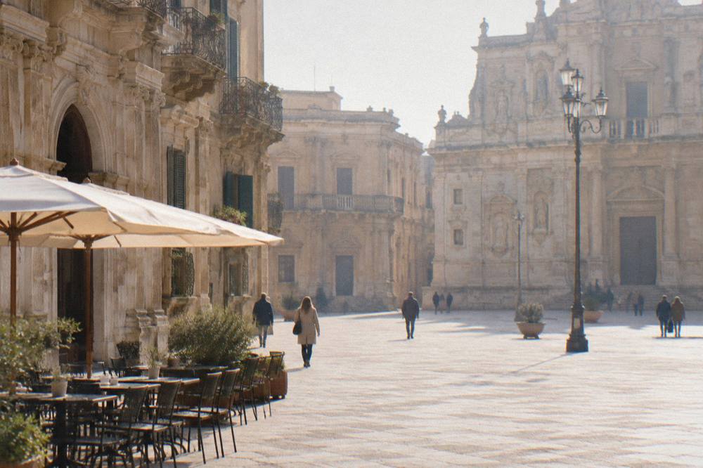 A wide Lecce piazza in late autumn with tables outside a cafe and few pedestrians