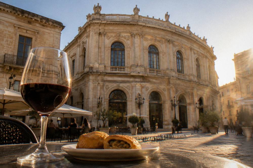 A small plate of savoury pastry and a glass of red wine on an evening cafe table