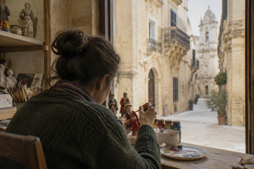 A visitor painting a small papier mache figure at a workshop bench in Lecce