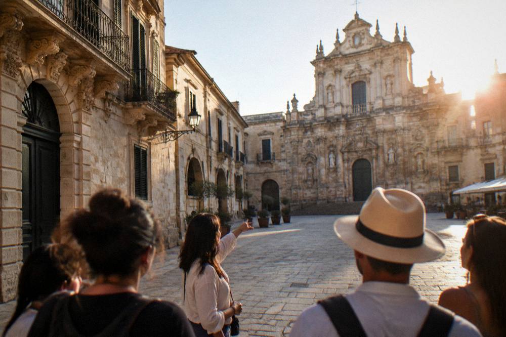 A walking guide showing a small group a historic Lecce square in late afternoon light