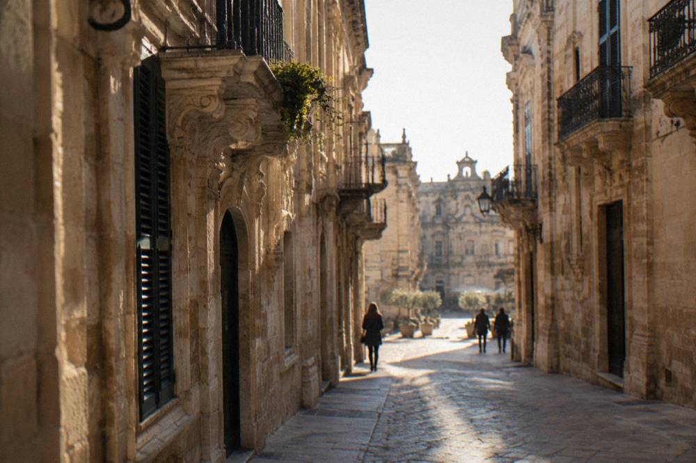 Narrow street in Lecce with golden stone walls lit by low evening sun